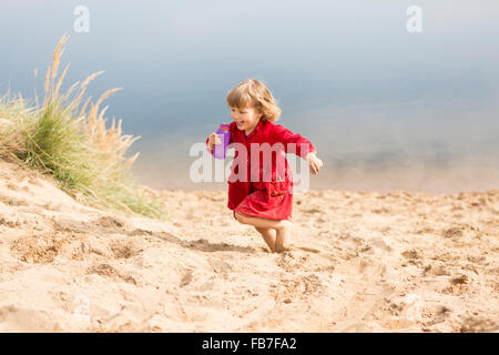 Cheerful girl holding water bottle while running on sand dune Stock Photo