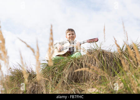 Low angle view of boy playing guitar on hill against sky Stock Photo