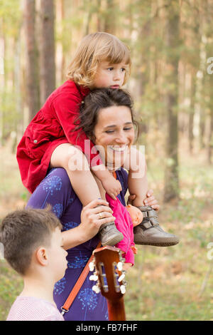 Happy woman carrying daughter while talking to son in forest Stock Photo
