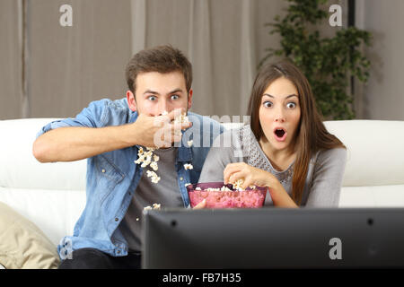 Amazed couple watching tv program sitting on a couch at home Stock Photo