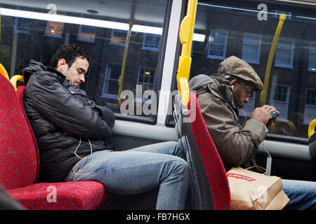 Two men listening to music on their phones on London bus Stock Photo