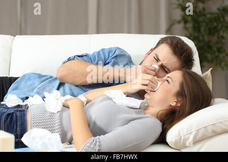 Ill couple sneezing in tissue lying on a couch at home. Flu concept Stock Photo
