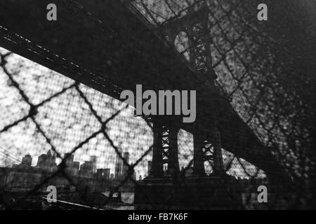 Distorted industrial view of Manhattan Bridge waterfront New York City through a wire safety fence. Monochrome, black and white image. Stock Photo