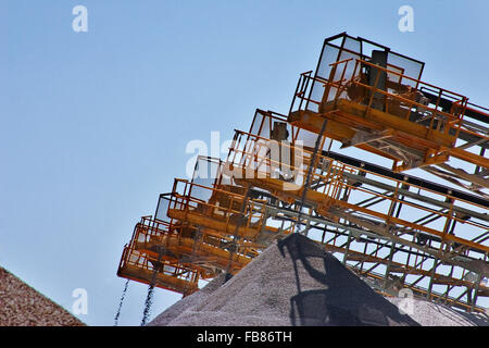 Crushed stone is sized then falls into piles from conveyor belts after being processed at a rock quarry. Stock Photo