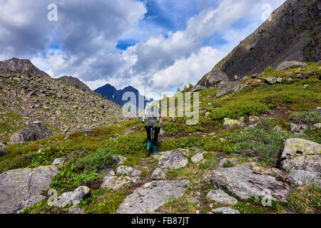 Hiking. Mountain tourism . A woman with a large backpack in rubber boots walks on a mountain path Stock Photo