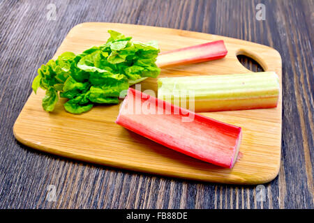 The stalks of rhubarb with green leaf on the planch on a dark wooden board Stock Photo