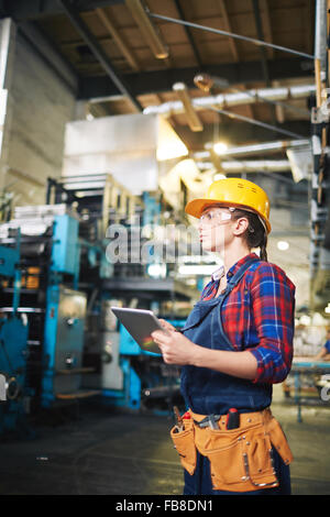 Young engineer in uniform and protective eyeglasses and helmet using touchpad Stock Photo