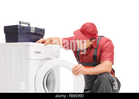 Young male plumber in a gray jumpsuit looking at a washing machine isolated on white background Stock Photo