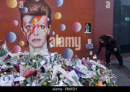 London 12th January 2016: Fans of iconic English music artist David Bowie who died from Cancer at the age of 69 on Sunday 10th January, gather to pay their respects at a makeshift shrine of flowers and tributes to the local boy from Brixton, south London. Commuters stopped-by before entering the nearby underground station to take pictures and silently remember their hero's great days playing the soundtracks of their childhoods. Richard Baker / Alamy Live News. Stock Photo