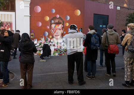 London 12th January 2016: Fans of iconic English music artist David Bowie who died from Cancer at the age of 69 on Sunday 10th January, gather to pay their respects at a makeshift shrine of flowers and tributes to the local boy from Brixton, south London. Commuters stopped-by before entering the nearby underground station to take pictures and silently remember their hero's great days playing the soundtracks of their childhoods. Richard Baker / Alamy Live News. Stock Photo