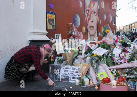London 12th January 2016: Fans of iconic English music artist David Bowie who died from Cancer at the age of 69 on Sunday 10th January, gather to pay their respects at a makeshift shrine of flowers and tributes to the local boy from Brixton, south London. Commuters stopped-by before entering the nearby underground station to take pictures and silently remember their hero's great days playing the soundtracks of their childhoods. Richard Baker / Alamy Live News. Stock Photo