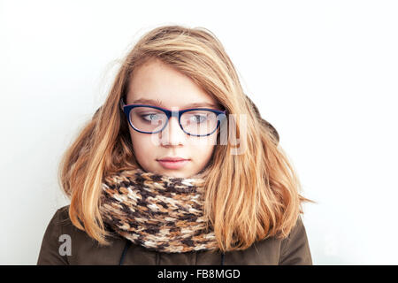 Closeup portrait of beautiful blond Caucasian teenage girl in glasses and warm scarf over white wall background Stock Photo