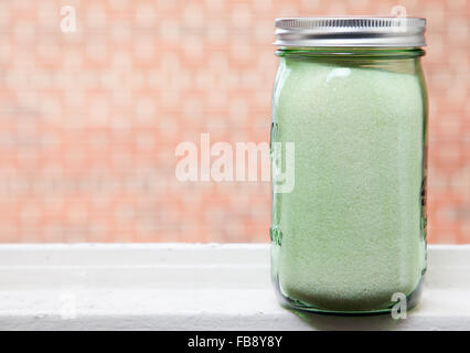 Organic granulated cane sugar in green mason jar, on windowsill with brick background. Stock Photo