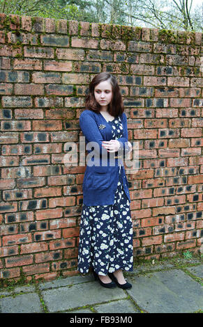 Young woman standing beside a brick wall looking worried dressed in a 1940s style Stock Photo