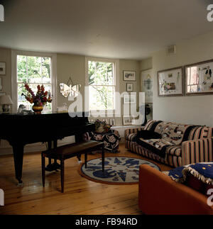 Grand piano and wooden flooring in nineties living room with a patterned throw on striped sofa Stock Photo