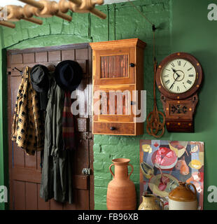 Coats hanging on pegs on back door of green nineties cottage kitchen with a small wall cupboard and wall clock Stock Photo