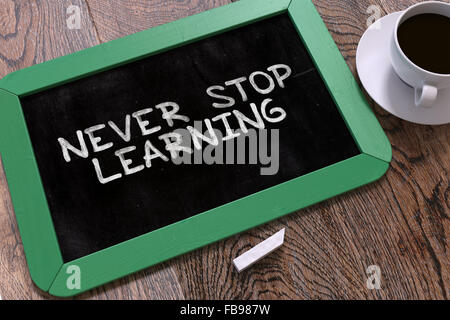 Never Stop Learning - Motivation Quote Handwritten on Green Chalkboard. Business Concept. Composition with Chalkboard and Cup of Stock Photo