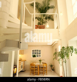 Wooden table and chairs in open plan double height kitchen and dining are with a potted palm on the mezzanine floor Stock Photo
