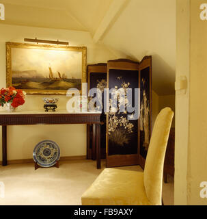 Large painting above console table in eighties hall with an antique folding screen and an upholstered cream chair Stock Photo