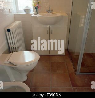 Vintage radiator beside basin and toilet in fitted vanity unit in shower room with terracotta tiled floor Stock Photo