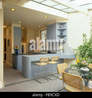 Chrome and wicker stools at breakfast bar in a modern kitchen with cantilevered chairs and glass table in the extension Stock Photo