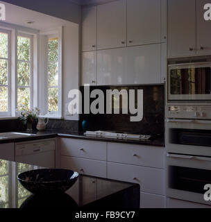 Black marble splash back above hob in a modern white kitchen with tall fitted units Stock Photo