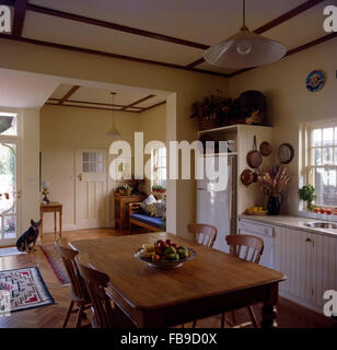 Vintage pine table and chairs in an open-plan traditional kitchen with a dog sitting beside the front door Stock Photo