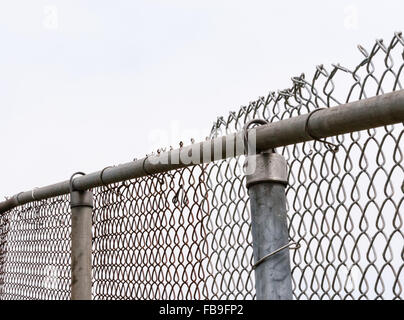 Top of old worn and damaged metal chain-link fence and posts against white sky. Stock Photo