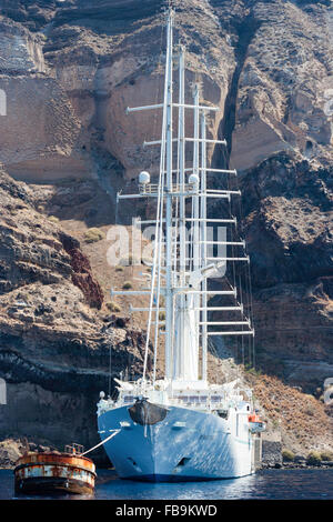 Santorini in Aegean sea. Ocean-going luxury four-masted yacht, 'wind spirit', operated by Windstar Cruises, moored under towering cliffs. Facing, bows. Stock Photo