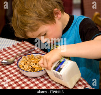 Child boy pouring milk on breakfast cereal at home Stock Photo