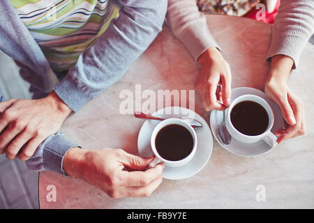 Close up of table and hands of young couple enjoying a cup of coffee at sidewalk restaurant Stock Photo