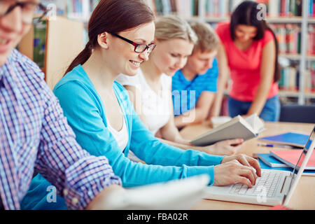 Smiling female student with laptop in library among her friends Stock Photo