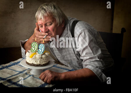 Old pensioner lighting his cigarette on his birthday cake. Stock Photo