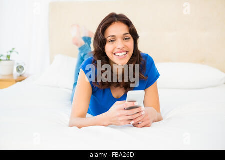 Smiling woman using smartphone while lying on bed Stock Photo