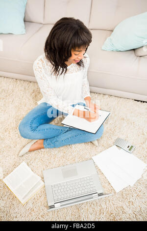 Casual woman writing notes while using laptop Stock Photo