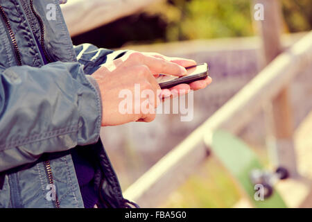closeup of a young caucasian man using a smartphone outdoors, next to his skateboard Stock Photo