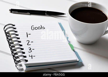 closeup of a notebook with a blank list of goals and a cup of coffee on a white wooden table Stock Photo