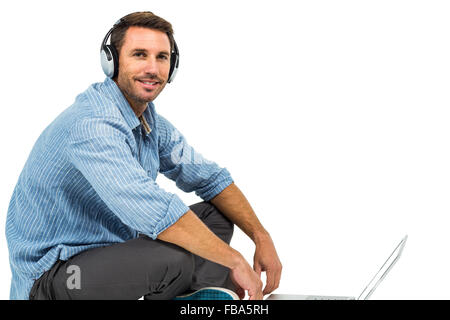 Portrait of man sitting on floor using laptop and headphones Stock Photo