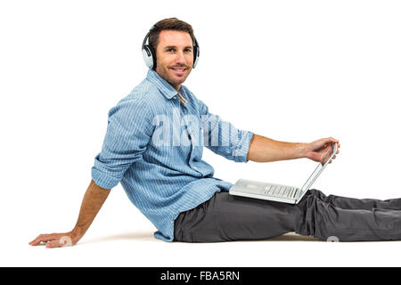 Happy man sitting on floor using laptop and headphones Stock Photo