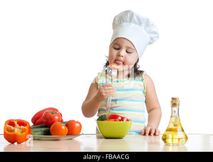 child girl in cook hat eating vegetables Stock Photo