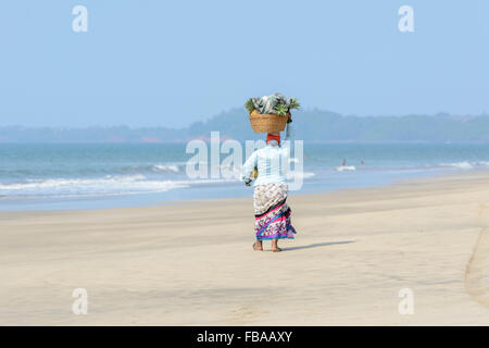 An Indian woman selling fruit and drinks walks along an empty beach, Mandrem beach, North Goa, India Stock Photo