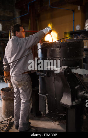 Steel worker in protective clothing raking furnace in an industrial foundry Stock Photo