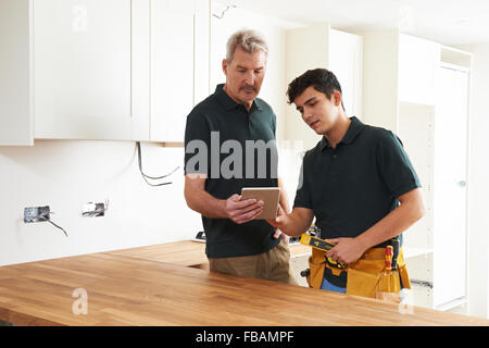 Carpenter And Apprentice With Digital Tablet Fitting Luxury Kitchen Stock Photo
