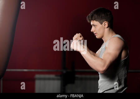 Young caucasian sportsman hit a punch bag, boxing, warming up in fitness center Stock Photo