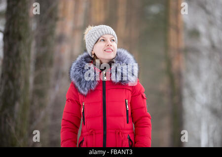 Beautiful girl in knitted hat and red winter coat with fur collar smiling dreamily outdoors Stock Photo