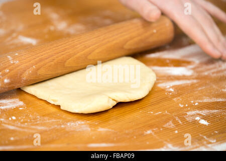 Close up homemade cooking, female hands roll out pastry with wooden dough roller on wooden table covered in flour Stock Photo