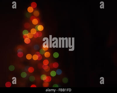 An abstract image featuring multi-colored light bokeh in the shape of a Christmas tree against a dark background. Stock Photo