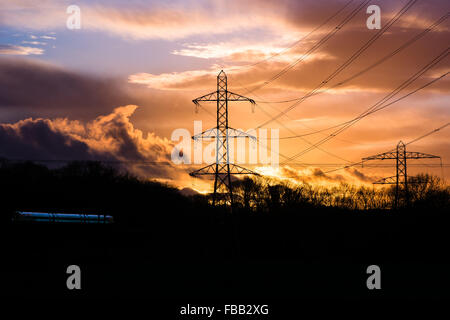 Industrial landscape with cables, train and sunset. Electricity cables and pylons are silhouetted in front of a sunset Stock Photo