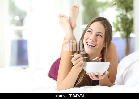 Healthy girl eating cereals at breakfast lying on the bed at home or hotel Stock Photo