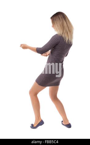 back view of standing girl pulling a rope from the top or cling to something. girl watching. Rear view people collection. backside view of person. Isolated over white background. Blonde in a short dress pulls the rope on the left. Stock Photo